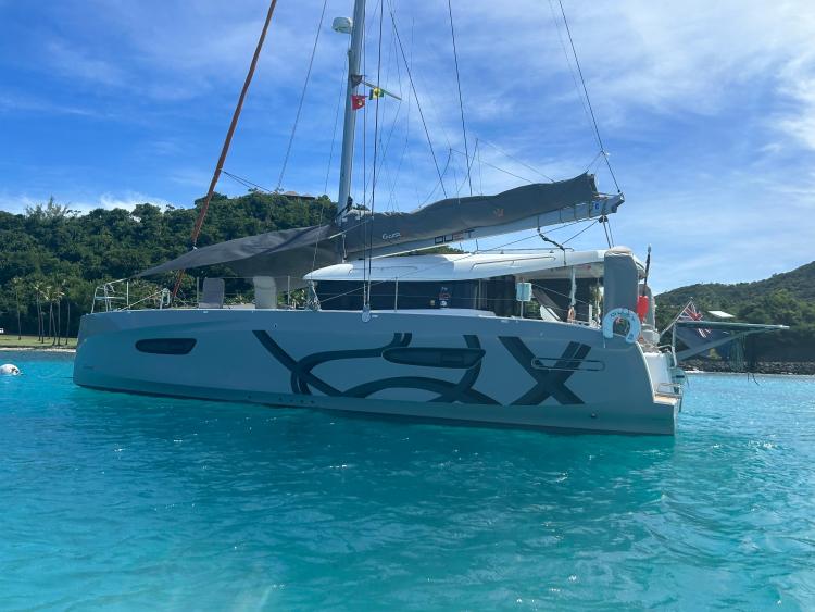 2024 Excess 14 catamaran sailing in clear blue waters near lush green island.