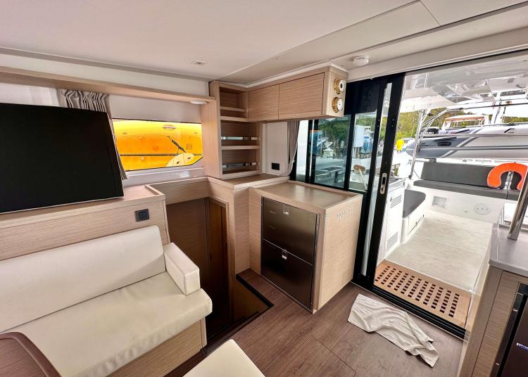 2023 Lagoon 46 yacht interior with modern seating, kitchenette, and sliding glass door to deck.