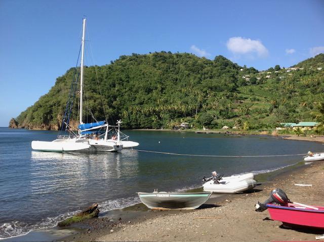Sailboat Polynésie 42 anchored near lush green island, small boats on sandy beach.