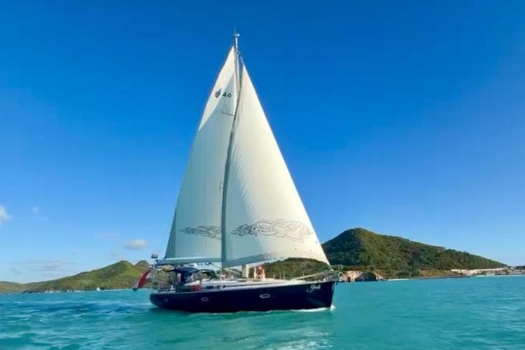 Bavaria Cruiser 46 sailboat on blue sea with green island backdrop.