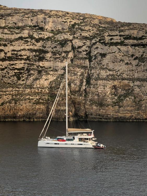 2019 Squalt Marine CK 64 catamaran sailing near rocky cliffs.