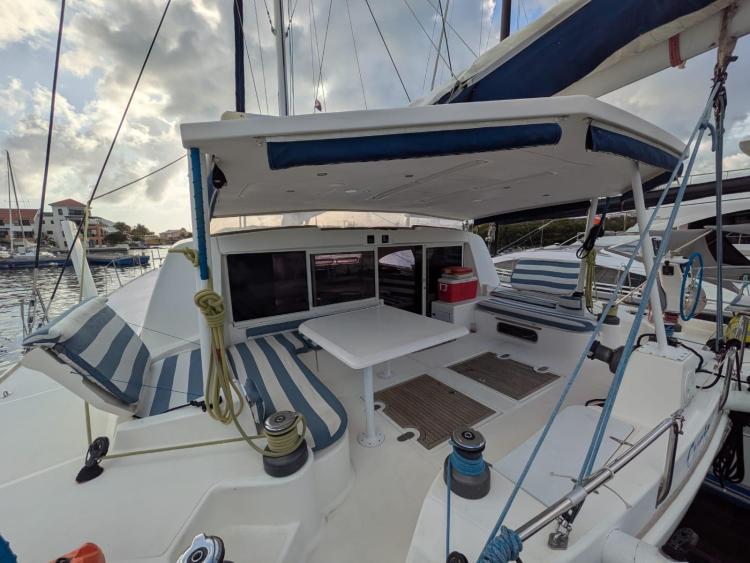 2012 Catana 55 yacht deck with seating, table, and striped cushions in a marina setting.