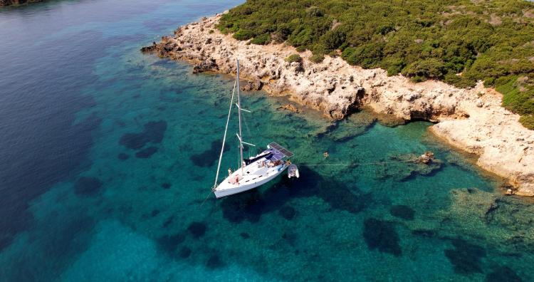 Sailboat Beneteau Cyclades 43.3 anchored in clear turquoise waters near rocky coastline, 2005 model.
