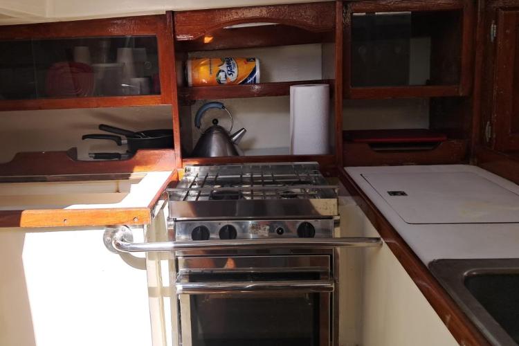 1986 Dufour CATALINA yacht kitchen with stove, wooden cabinets, and kettle.