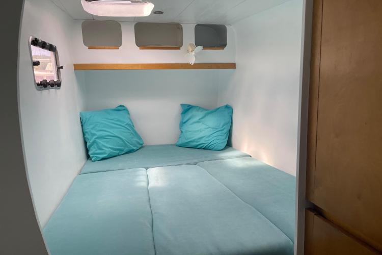 Compact cabin interior with turquoise bedding, small window, and overhead storage in Custom KSENIA 149, 2010.