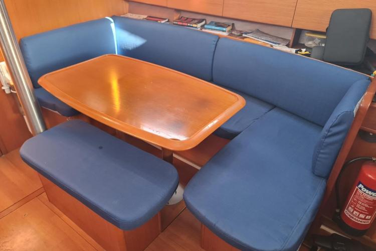 Interior of 2005 Beneteau Cyclades 43.3 yacht with blue cushioned seating and wooden table.