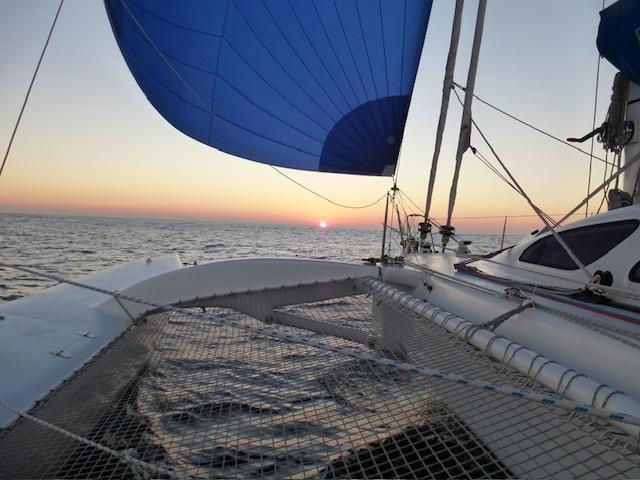 Sailing at sunset on a 2005 Custom Polynésie 42 catamaran with blue sails.