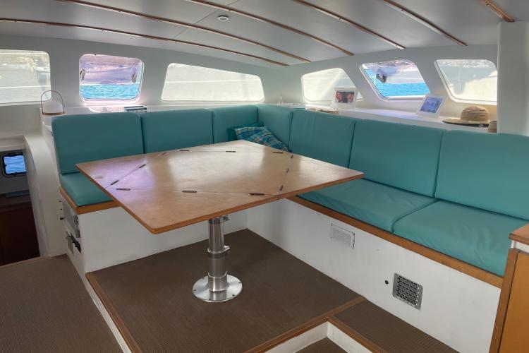 Spacious boat interior with teal seating, wooden table, and large windows. Custom KSENIA 149, 2010.