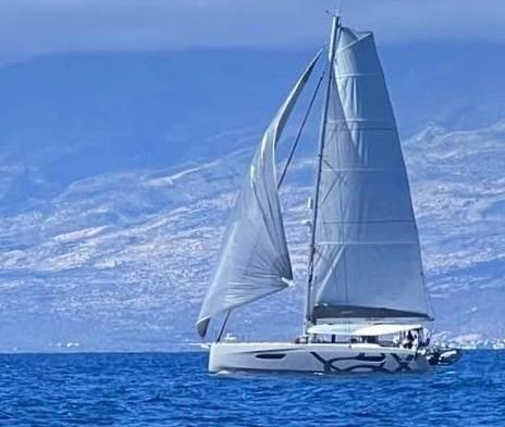 2024 Excess 14 sailboat navigating blue waters with mountainous backdrop.