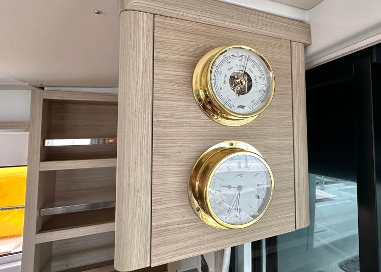 Wooden panel with brass barometer and clock on 2023 Lagoon 46 yacht interior.
