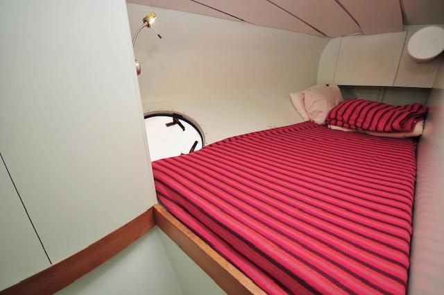 Cozy cabin interior of 2005 Custom Polynésie 42 with striped bedding and porthole.